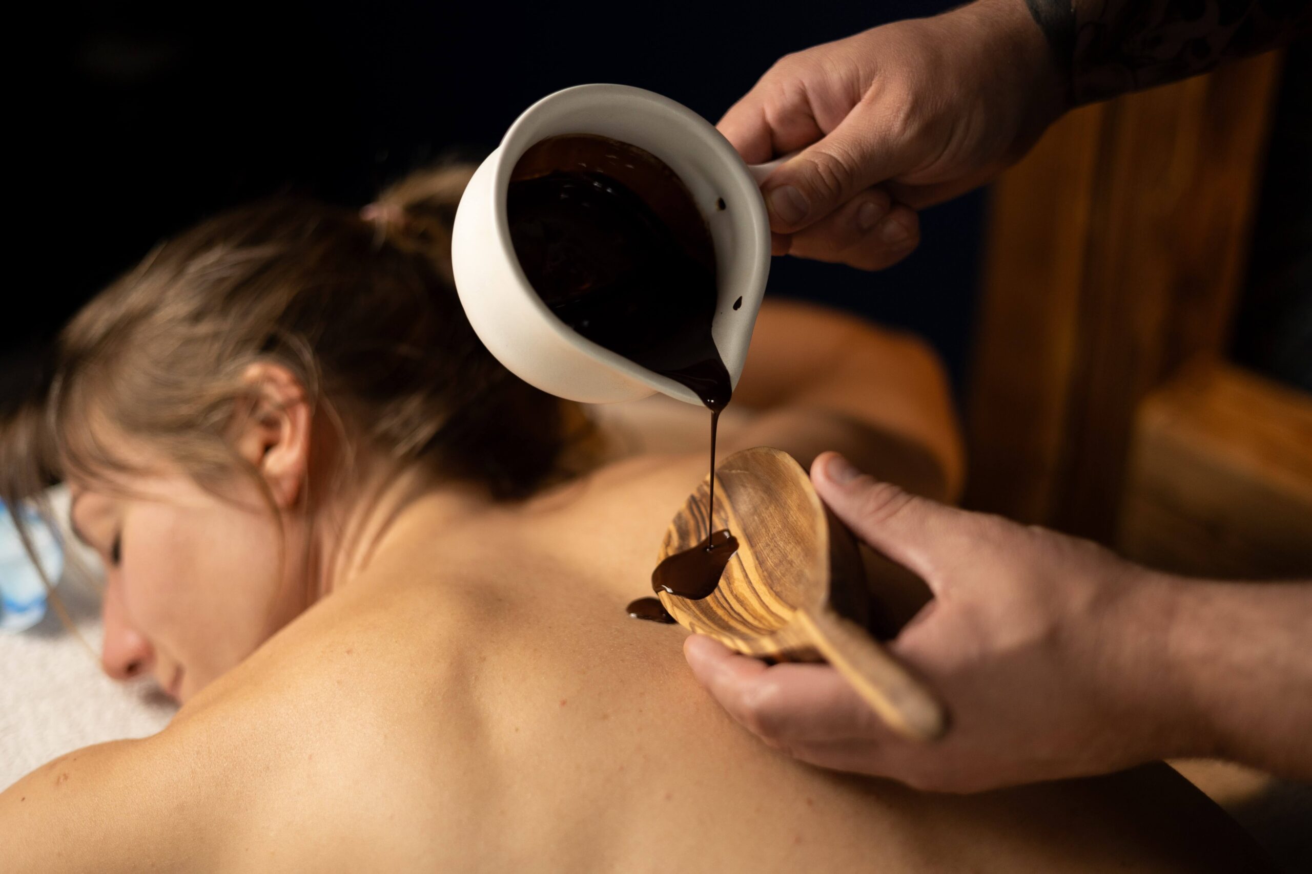 Zdjęcie przedstawia masażystę wykonującego masaż ciepłą czekoladą w gabinecie Oriental SPA w Jeleniej Górze. Masażysta aplikuje ciepłą, płynną czekoladę na plecy pacjenta, stosując techniki masażu, które nawilżają skórę, relaksują ciało i poprawiają samopoczucie.